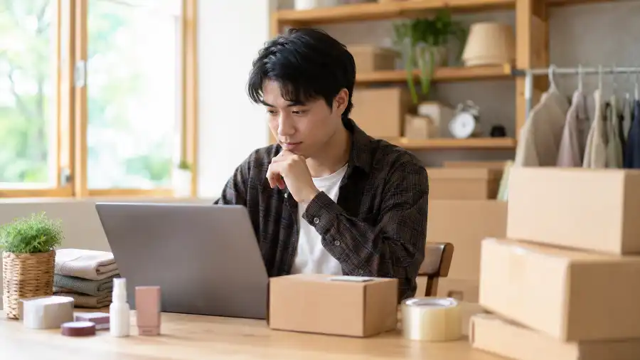 Chủ shop online xem các gói KlingAI để làm video quảng cáo bên cạnh thùng hàng